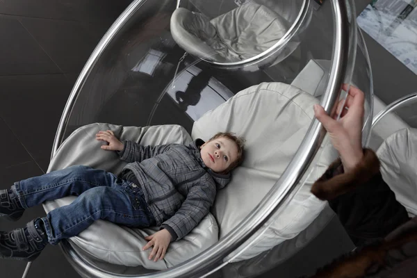 Child relaxes in glass chair — Stock Photo, Image