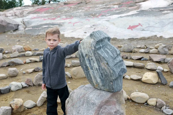 Boy touching face carved in stone, Karelia