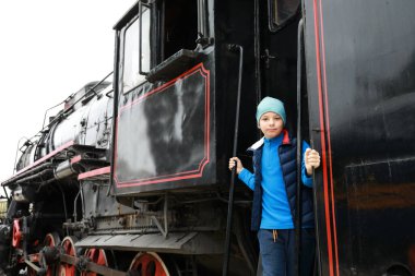Tren istasyonunda buharlı lokomotifin basamağındaki çocuk