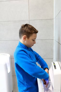 Çocuk tuvalette kurutma makinesiyle ellerini kurutuyor.