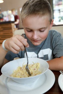 Çocuk restoranda peynirli makarna yiyor.