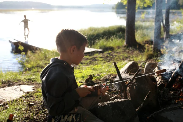 少年は森の中で火の上にソーセージをフライパン カレリア — ストック写真