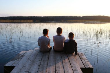 Çocuklar gün batımında gölün kenarındaki tahta köprüde dinleniyorlar, Karelia.