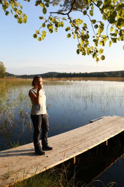 Göl kenarındaki tahta köprüde çay içen kadın, Karelia.
