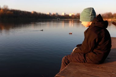 Gün batımında gölün kenarındaki çocuğun portresi.