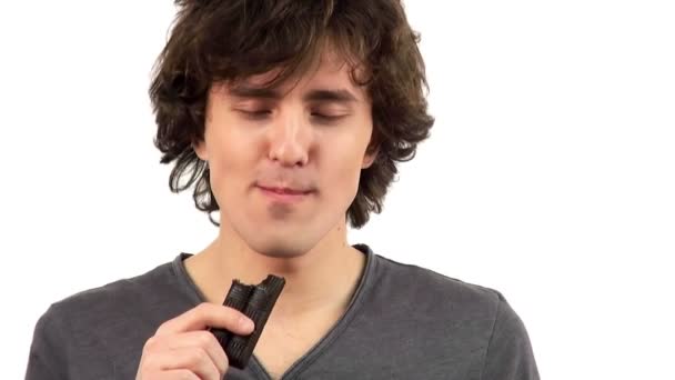 Χαρούμενος νεαρός άνδρας τρώει σοκολάτα, απομονώνονται σε λευκό φόντο — Αρχείο Βίντεο