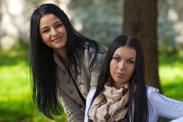 Två glada, vackra flickor sitter i parken på en sommardag — Stockfoto