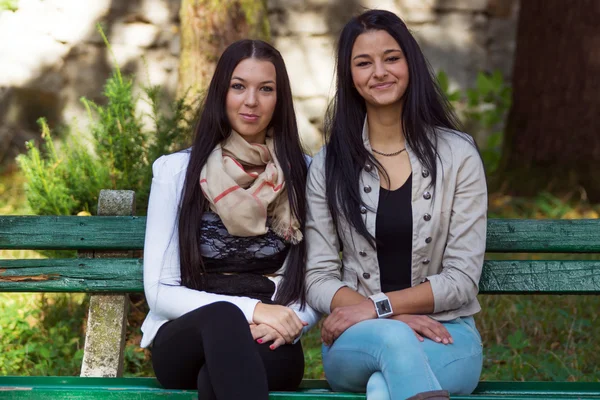 Två glada, vackra flickor sitter i parken på en sommardag — Stockfoto