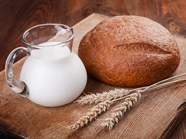 Pão e leite em um jarro de vidro em uma mesa de madeira — Fotografia de Stock