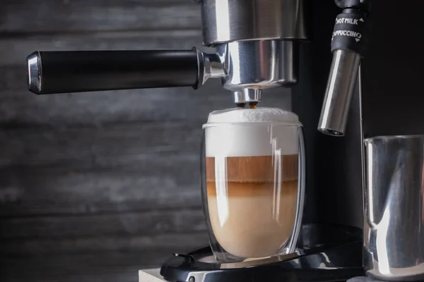 Koffie latte macchiato wordt gegoten in een glazen beker in een koffiezetapparaat — Stockfoto