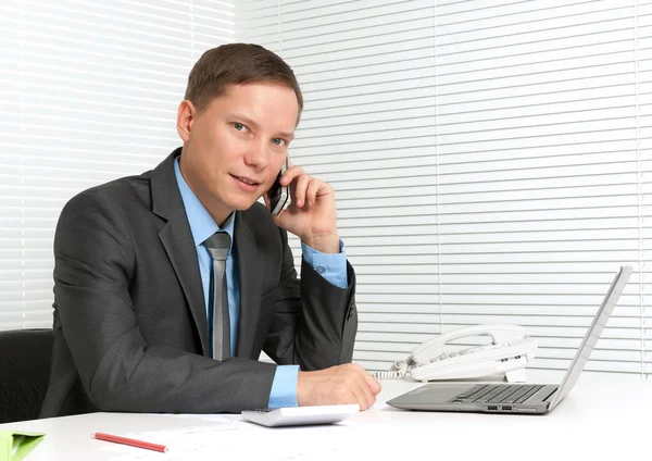 Vrolijke jonge zakenman met behulp van mobiele telefoon op Bureau — Stockfoto