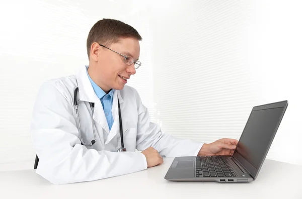 Médico sentado em sua mesa com computador portátil — Fotografia de Stock