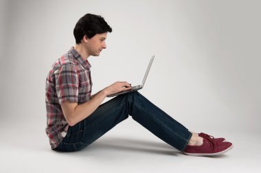 adam oturmuş ve bir dizüstü bilgisayar kullanarak