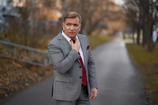40歳の男性は灰色のスーツと赤いネクタイを路上で着ています — ストック写真