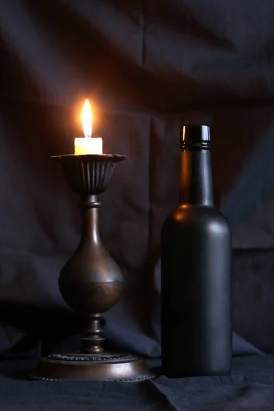 Schwarze Glasflasche Neben Brennender Kerze Vor Schönem Dunklen Textilen Hintergrund — Stockfoto