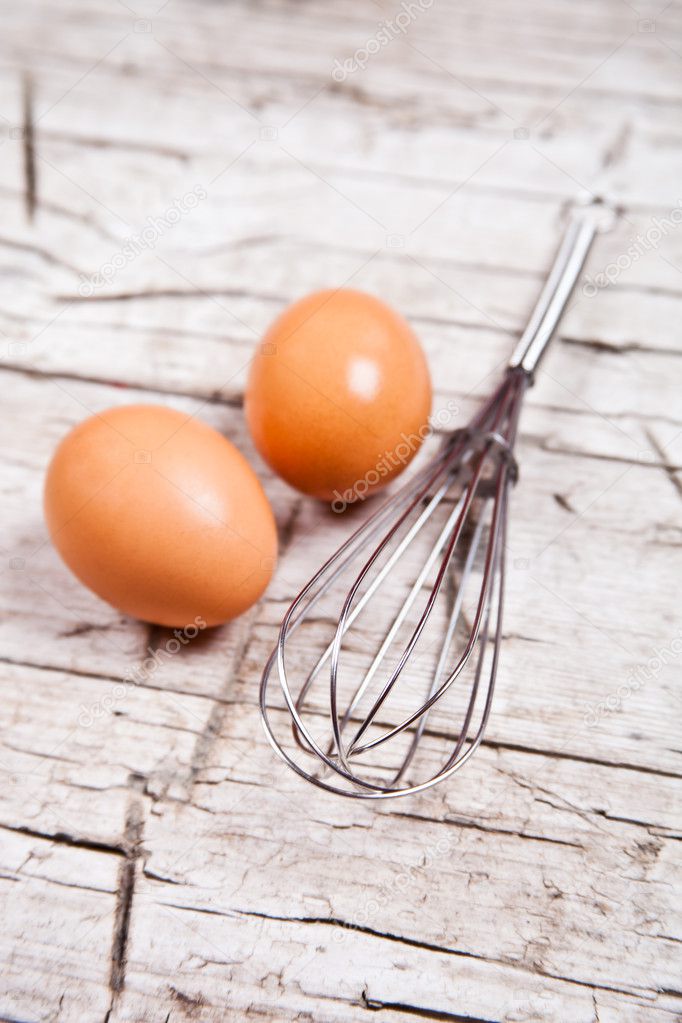 wire whisk and two brown eggs