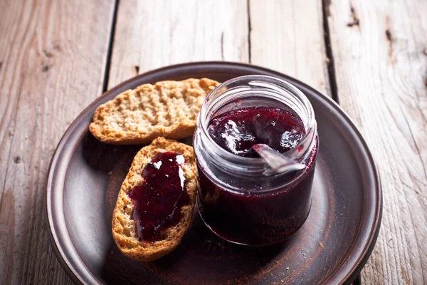 Black currant jam in glass jar and crackers — Stock Photo, Image