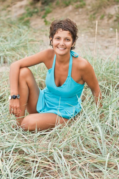 Brunet woman in blue sitting in a grass — Stock Photo, Image