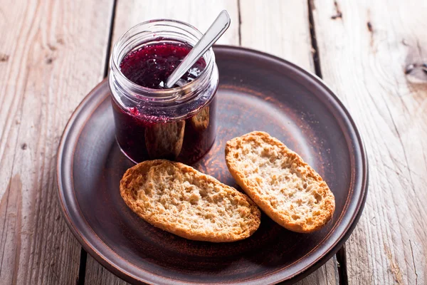 Black currant jam in glass jar and crackers — Stock Photo, Image