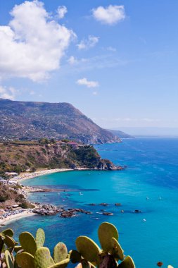 Turkuaz körfezi, kumlu sahil, yeşil dağlar ve bitkiler, mavi gökyüzü beyaz bulutlar arka plan, uçurum platformu Capo Vaticano Cape, Calabria, Güney İtalya.