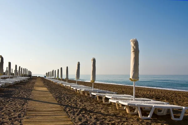 Een aantal plank ligbedden en parasols op een strand — Stockfoto