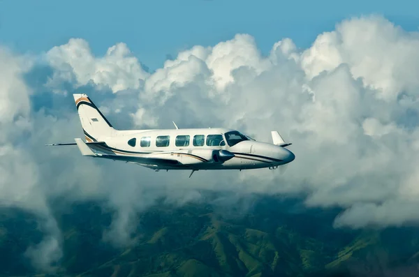 O avião voador contra nuvens e colinas verdes — Fotografia de Stock
