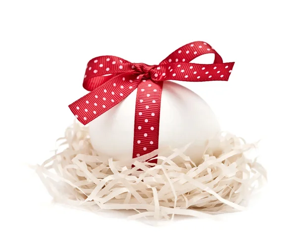 Белое яйцо в гнезде с красной лентой и луком — стоковое фото