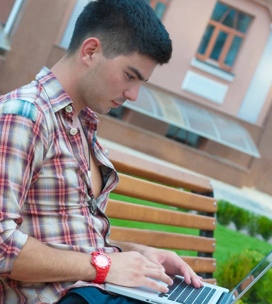 Jovem com um laptop no banco . — Fotografia de Stock