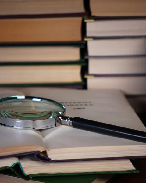 Magnifying glass on a pile of open books. — Stock Photo, Image