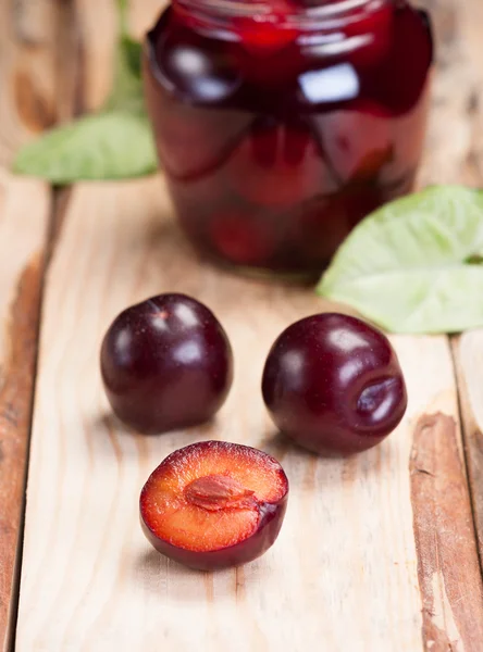 Pflaumen auf grobem Holztisch. im Hintergrund Glas mit Marmelade. — Stockfoto