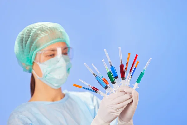 Mujer joven doctora con muchas jeringas multicolores en las manos en blu — Foto de Stock