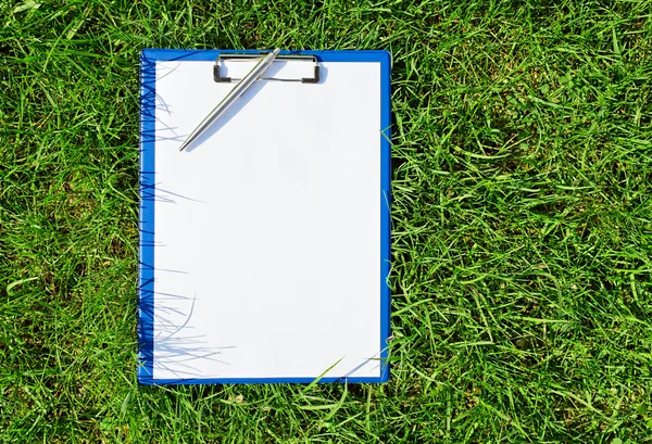 Blue medical clipboard with a pen over lush green grass — Stock Photo, Image