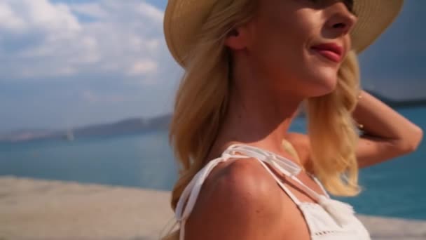 Vrouw in de zon strohoed zittend op een houten bank op blauwe zee achtergrond bij Ermioni. Griekenland — Stockvideo