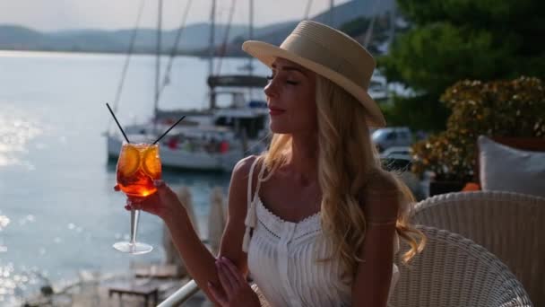 Vrouw met strohoed drinkt aperol Spritz cocktail zittend op zomerterras in Ermioni, Griekenland — Stockvideo