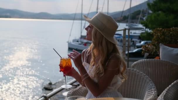 Mujer con sombrero de paja bebiendo aperol Spritz cóctel sentado en la terraza del café de verano en Ermioni, Grecia — Vídeos de Stock