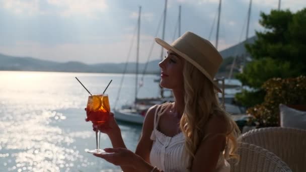 Vrouw met strohoed drinkt aperol Spritz cocktail zittend op zomerterras in Ermioni, Griekenland — Stockvideo