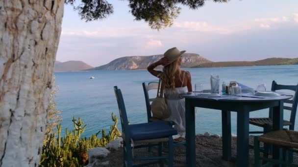 Hermosa chica turística sentada en la cafetería de verano con el mar y las montañas en el fondo en Ermioni, Grecia — Vídeos de Stock