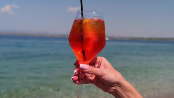 Γυναικείο χέρι κρατώντας ποτήρι Aperol Spritz κοκτέιλ σε φόντο θάλασσας — Αρχείο Βίντεο