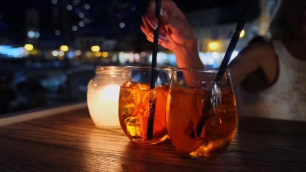 Vrouw die aperol Spritz cocktail drinkt zittend op zomerterras 's avonds in Hydra, Griekenland — Stockvideo