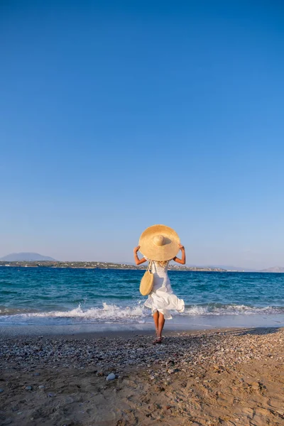 Aantrekkelijke jonge vrouw dragen jurk staan aan zee kust met handen opgeheven — Stockfoto
