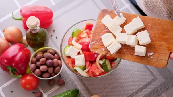 Grieks salade voorbereiding serie concept - vrouw gieten gesneden feta kaas in een kom — Stockvideo