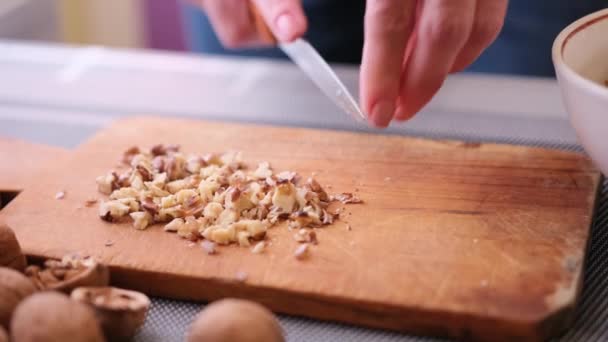 Hakken van walnoten kernen met keukenmes op een hout snijplank — Stockvideo