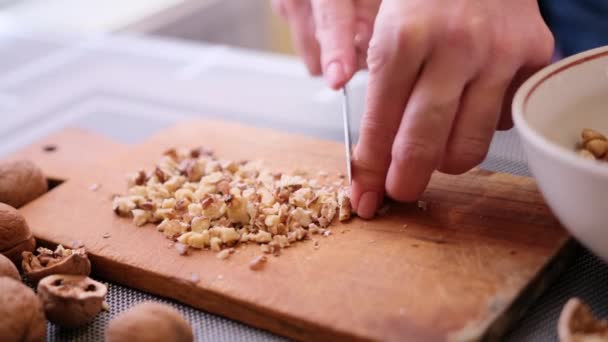 Hakken van walnoten kernen met keukenmes op een hout snijplank — Stockvideo