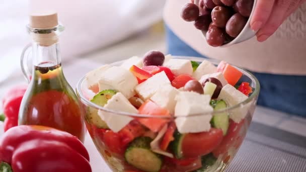 Greek salad preparation series concept - γυναίκα ρίχνει ελιές σε μπολ με ψιλοκομμένα λαχανικά — Αρχείο Βίντεο