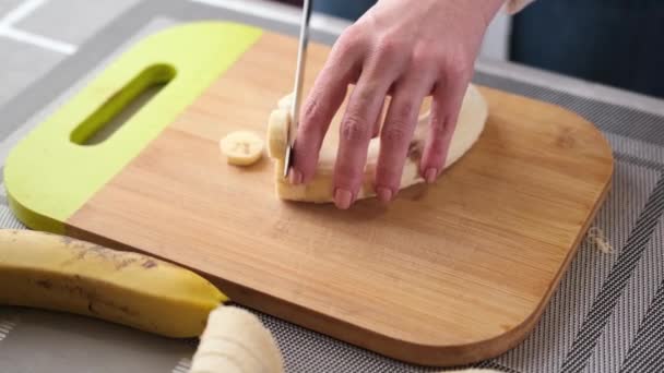 Žena krájí žlutý banán na dřevěné řezací desce pro náplň dortů — Stock video