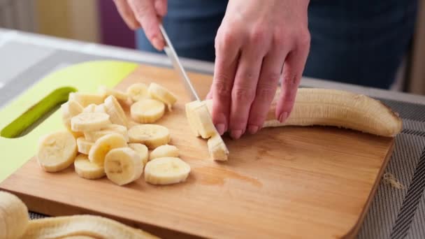 Kvinna skivning den gula banan på trä skärbräda för tårta fyllning — Stockvideo