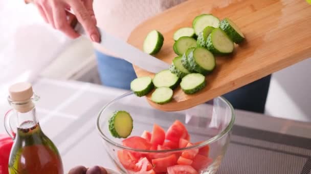 Grieks salade voorbereiding serie concept - vrouw gieten gesneden komkommers in een kom — Stockvideo