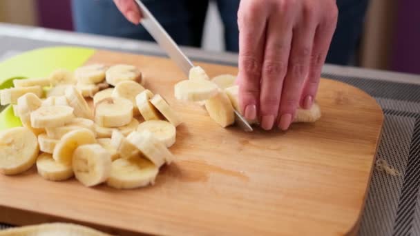 Kvinna skivning den gula banan på trä skärbräda för tårta fyllning — Stockvideo
