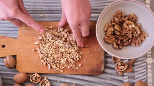 Hakken van walnoten kernen met keukenmes op een hout snijplank — Stockvideo