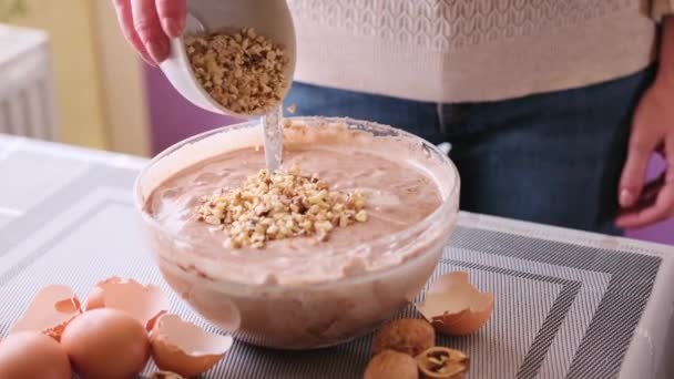 Making walnut chocolate cake - adding walnuts to raw dough in a glass bowl — Vídeos de Stock
